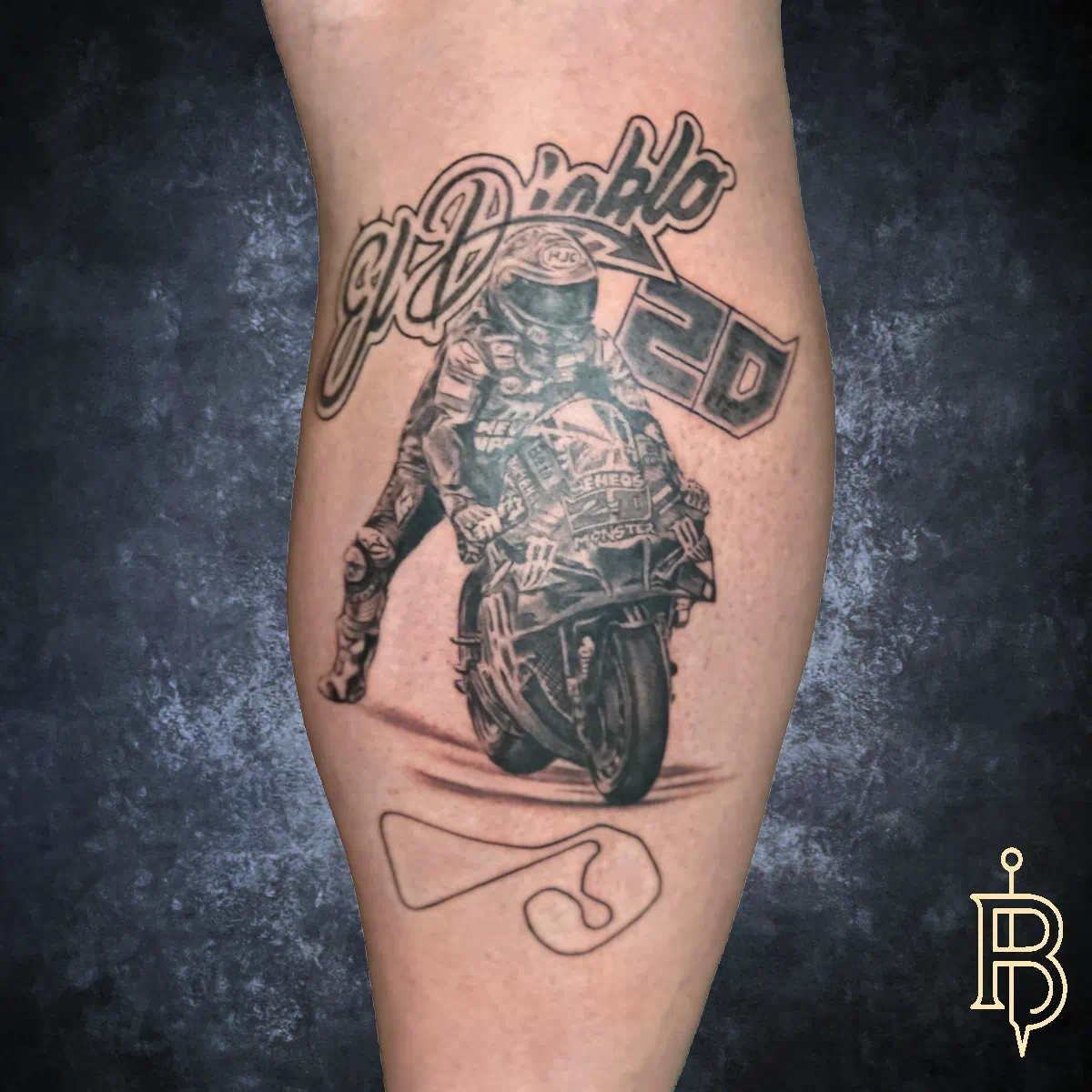 Detailreiches Bein-Tattoo: Rennfahrer auf Motorrad mit der Aufschrift ‚El Diablo‘ und der Startnummer 20, darunter eine stilisierte Rennstrecke, in schwarzgrauen Schattierungen.